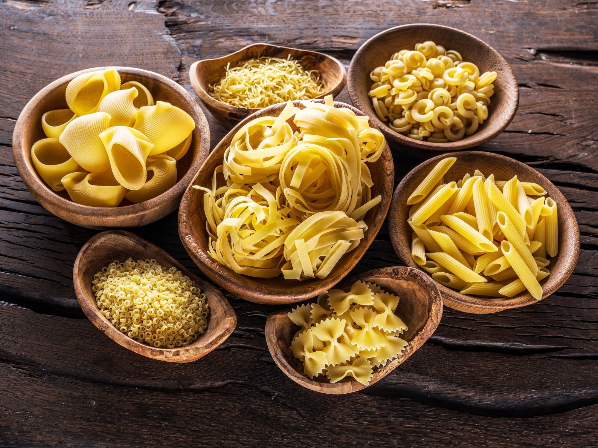 Different pasta types in wooden bowls on the table. Top view.